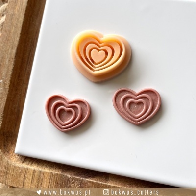 Cortadores de plástico em forma de corações concêntricos junto a tabuleiro branco com borda de madeira