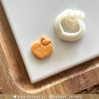 cortador de biscoitos em forma de pêssego com biscoito laranja em superfície branca e tábua de madeira