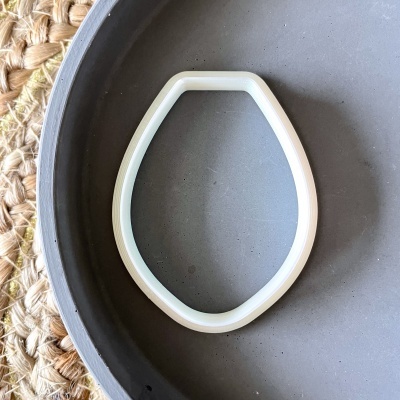 Forma de silicone branca em forma de lágrima sobre prato cinza em superfície de corda entrelaçada