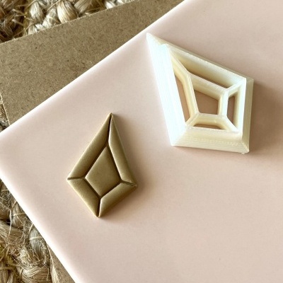 Dois objetos geométricos losango, um bege liso e outro branco tridimensional, sobre superfície rosa clara