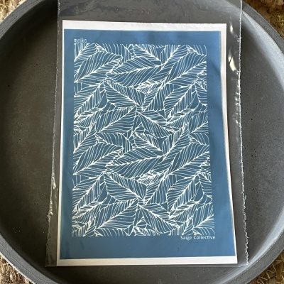 Cartão com padrão de folhas brancas sobre fundo azul, embalado em plástico transparente