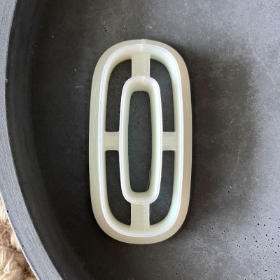 Clip branco oval com barras transversais sobre prato preto texturizado