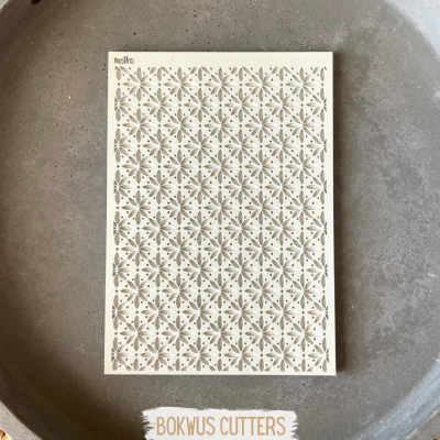 tábua retangular branca com padrão floral recortado sobre superfície cinzenta redonda