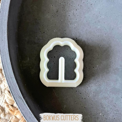 Cortador de massa em forma de árvore branca com bordas onduladas sobre superfície escura