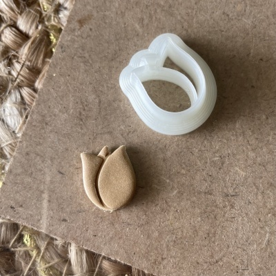 Cortadores de massa para bolachas em forma de tulipa, branco e bege, sobre cartão castanho e tapete de corda.