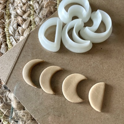 Peças de joalharia semicirculares brancas e bege sobre superfície castanha e tapete de fibras naturais