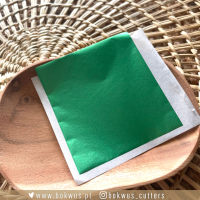 Pacote verde com borda branca em prato de madeira sobre superfície trançada