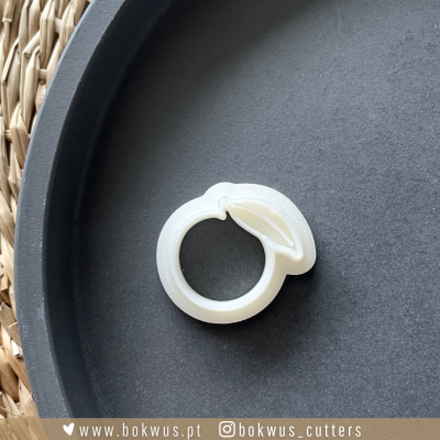 Cortador de bolos branco em formato de fruta, sobre prato preto com borda de rattan visível