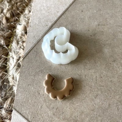 Moldes de corte brancos e castanhos em arcada ondulada sobre superfície castanha com tecido natural ao lado