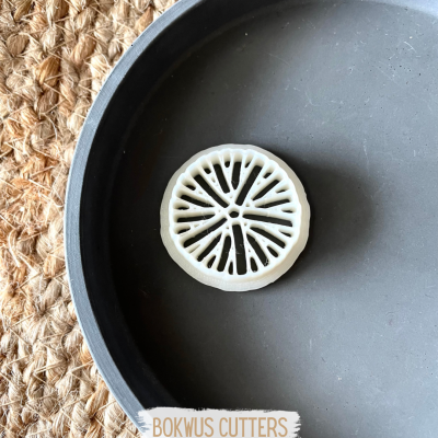 Cortador de massa branco com padrão circular, em prato preto sobre esteira de fibra natural