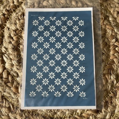 Stencil azul com flores brancas em saco plástico sobre superfície de fibra têxtil trançada