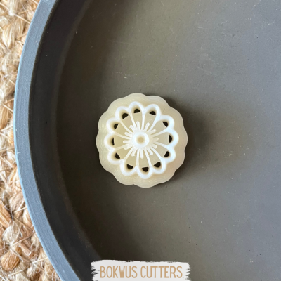 Cortador de biscoitos branco com padrão circular, sobre superfície escura, com etiqueta BOKWUS CUTTERS