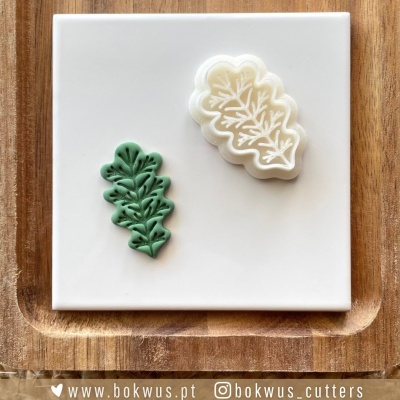 Dois cortantes em formato de folha, verde e branco, sobre azulejo branco e base de madeira.