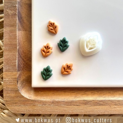 Cortantes de pastelaria em forma de folhas em verde e laranja com molde branco sobre placa branca e tabuleiro de madeira