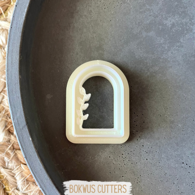 Cortante para bolachas branco em forma de arco com folhas, numa bandeja cinzenta.