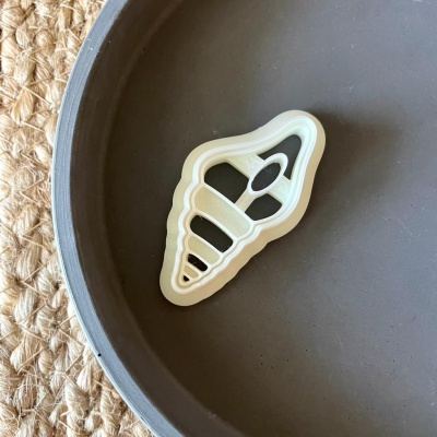 Cortador de bolachas em forma de sorvete branco sobre prato cinzento num tapete de fibras trançadas