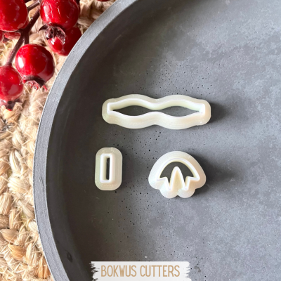 Três cortadores de biscoitos em plástico branco sobre prato cinzento com bagas vermelhas ao lado.