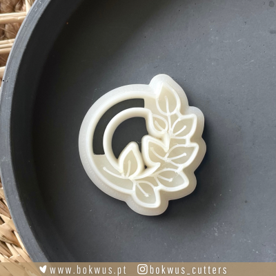 Cortador de biscoitos branco com design de folhas e círculos num prato preto