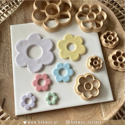 Cortadores de massa de madeira em forma de flor com massas coloridas correspondentes sobre prato branco