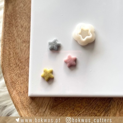 Cortadores de massa em forma de estrela de várias cores sobre superfície branca e base de madeira
