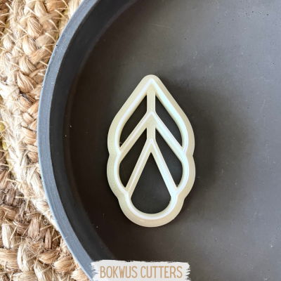 Cortante para bolachas em forma de folha branca num prato cinzento sobre superfície de ráfia.