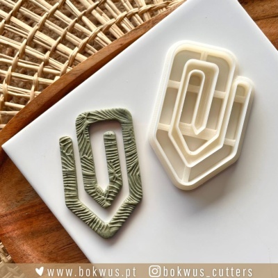 Cortadores de massa em plástico branco com peça de massa verde texturada em formato de clipe