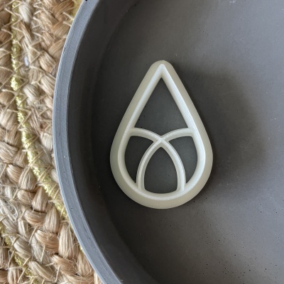 Forma branca de cortar biscoitos em formato de gota em prato cinza com esteira de fibras naturais