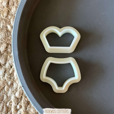 Dois cortadores de biscoito brancos em forma de roupa íntima sobre prato cinzento