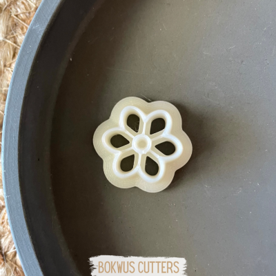 Cortador de biscoitos branco em forma de flor sobre superfície preta redonda