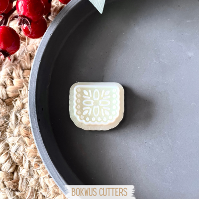 Cortador de massa branco e bege com padrão floral num prato cinzento sobre ráfia e bagas vermelhas