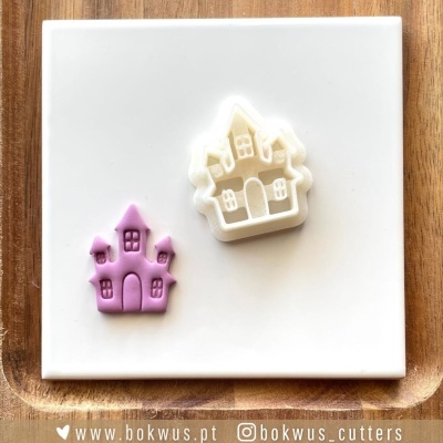 Dois cortadores de biscoitos em formato de castelo, branco e lilás, sobre placa branca em madeira