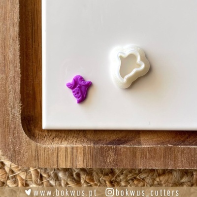 Dois cortadores de massa em forma de mão, um branco e outro roxo, em superfície branca com base de madeira