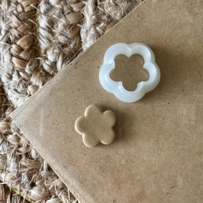Cortador de biscoitos branco em forma de flor com massa dourada cortada no mesmo formato sobre fundo castanho e tapete de fibras naturais