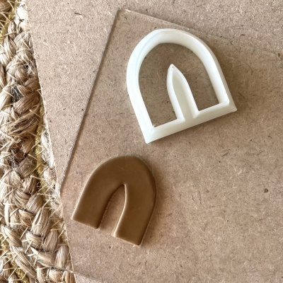 Cortador branco e peça de pasta modelável castanha em forma de arco sobre superfície de madeira