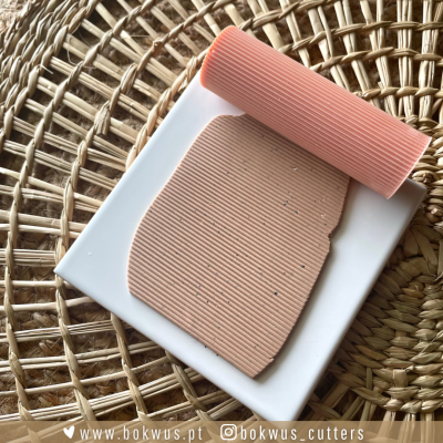 Rolo de texturização rosa e massa com textura de linhas finas sobre base branca e superfície de palha