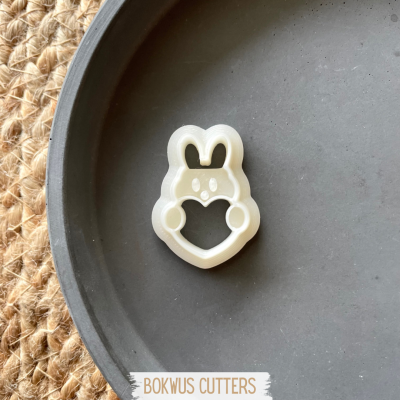 Cortador de biscoitos branco em forma de personagem com orelhas de coelho numa bandeja cinzenta.