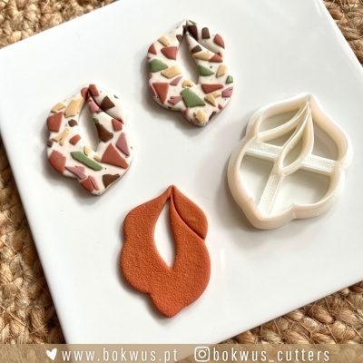 Cortador de massa em formato de folha e peças de massa modelada coloridas e castanhas sobre prato branco