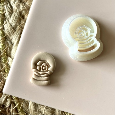 Carimbo branco em forma de bola de neve com casa, e respetiva impressão em argila bege numa superfície rosa