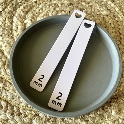 Dois espessímetros metálicos prateados marcados 2 mm sobre prato cinzento em base de fibra natural