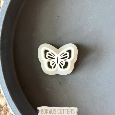 Molde ou cortador de biscoitos em forma de borboleta branco sobre superfície cinzenta redonda