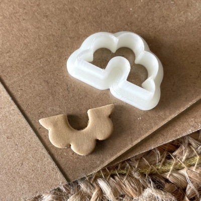 Cortador de massa branco em forma de nuvem com efeito ondulado e pedaço de massa clara ao lado.