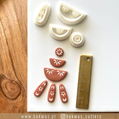 Cortantes para pastelaria em plástico branco com desenhos florais e régua dourada numa superfície branca