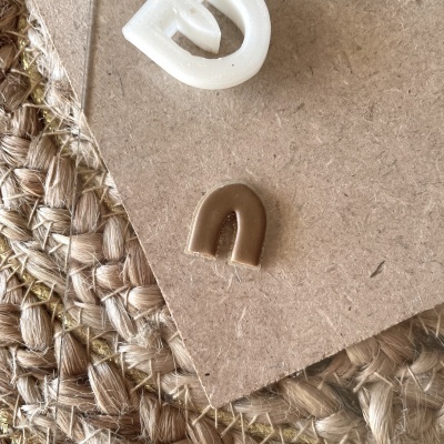 Brincos pequenos em forma de arco branco e castanho sobre cartão reciclado e tecido trançado