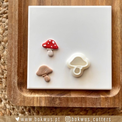 Cortador de bolachas de cogumelo com bolachas decoradas sobre placa branca e tábua de madeira