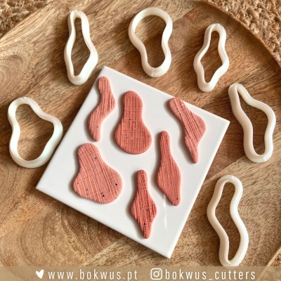 Cortadores de massa em plástico branco e peças texturizadas cor de rosa sobre prato branco e madeira.