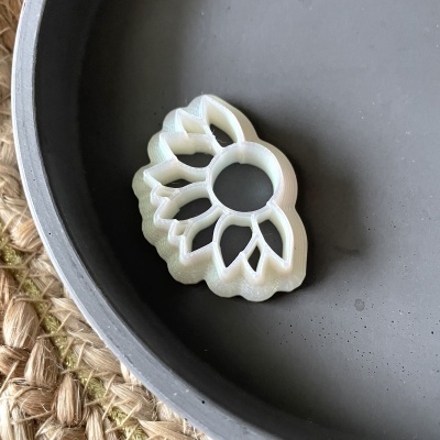 Anel branco com formato de pétalas dentro de prato cinza fosco sobre superfície trançada