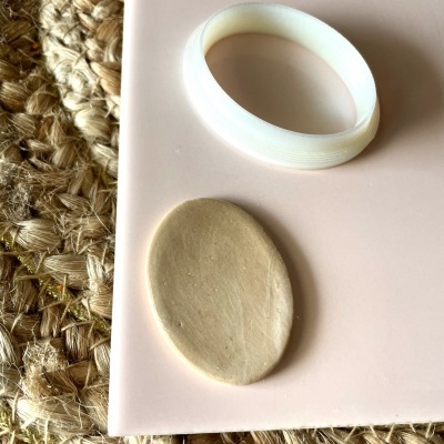 Pulseira branca e objeto oval bege sobre superfície rosa em base de fibra natural