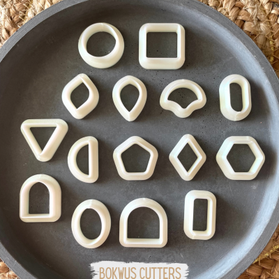 Conjunto de cortadores de biscoito brancos em diferentes formas geométricas numa travessa cinza