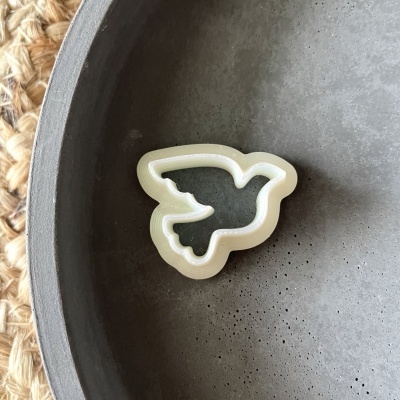 Mini cortador de biscoitos em forma de pomba branco dentro de prato cinzento