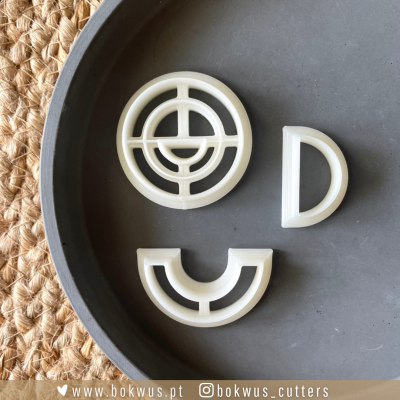 Três cortadores de plástico branco em formas geométricas sobre placa preta e superfície têxtil